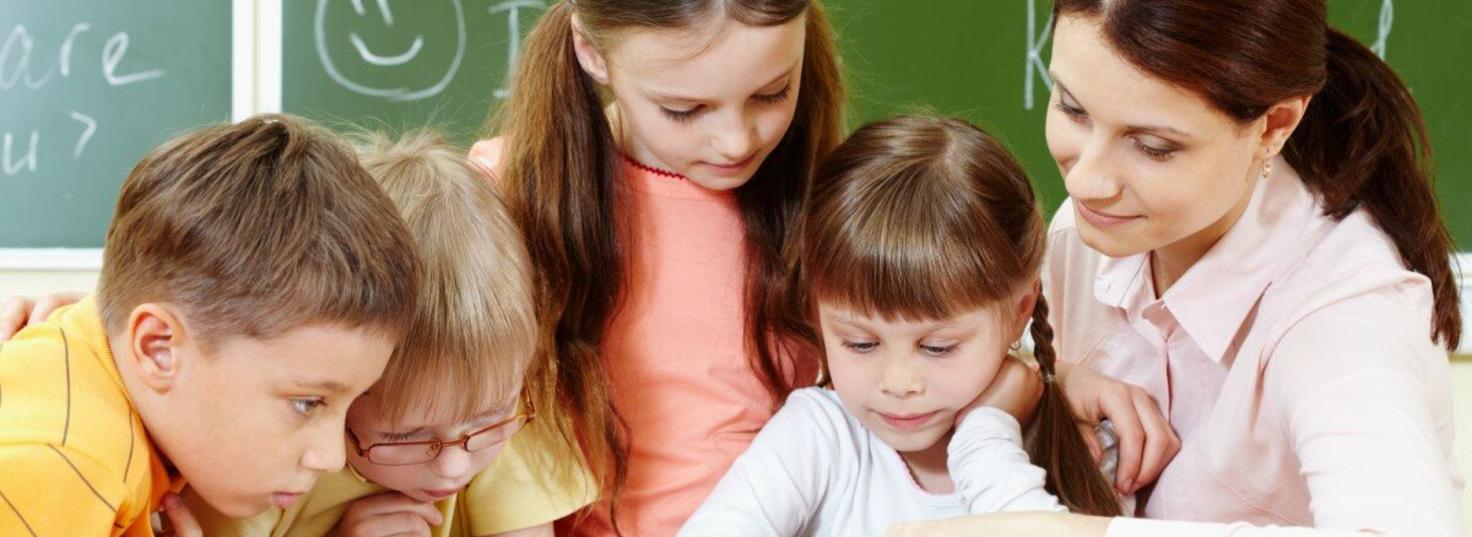Три девочки и мальчик в классе перед зелёной школьной доской читают  книгу